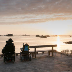 handicapped couple in wheelchairs enjoy a beautiful ocean sunset
