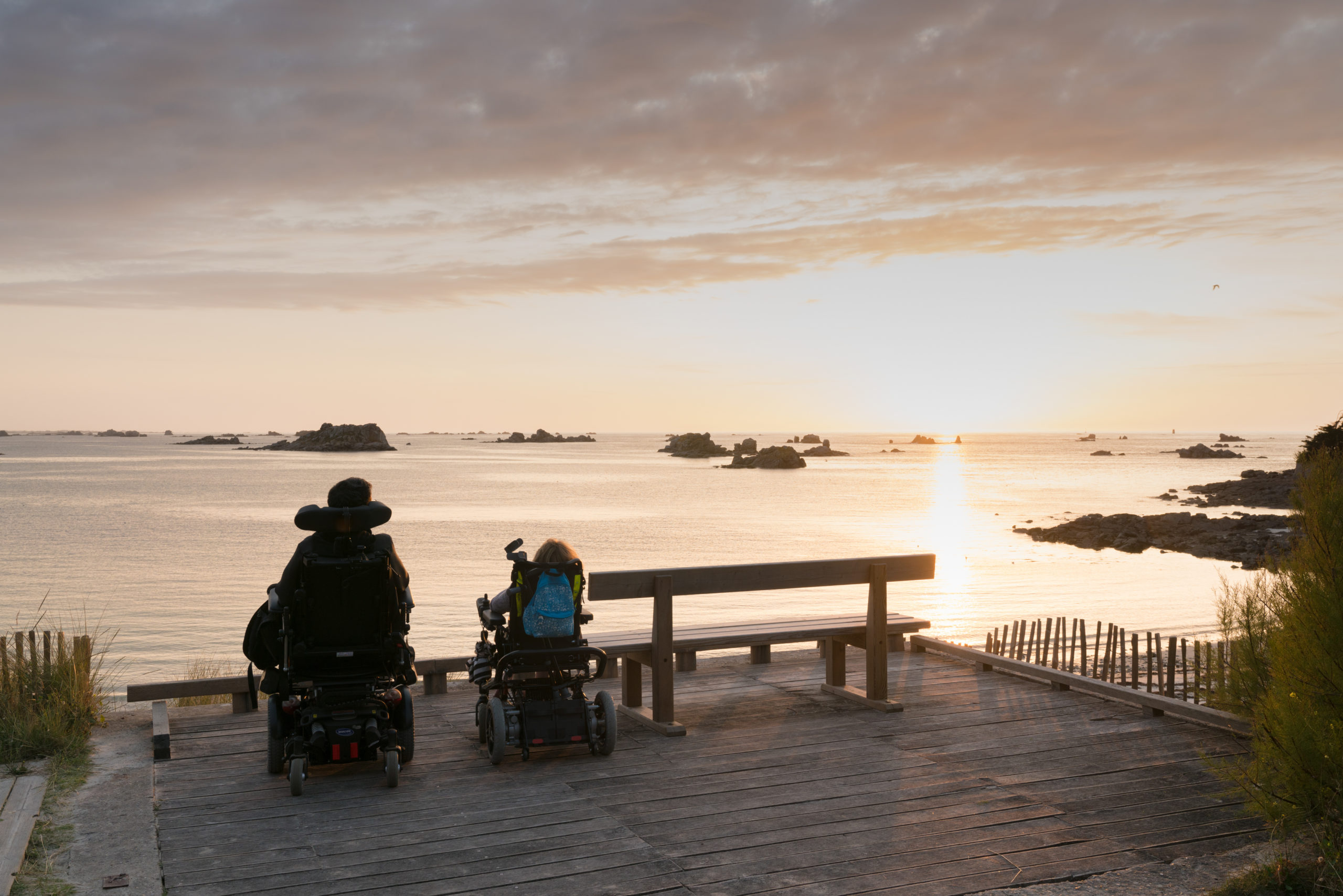 handicapped couple in wheelchairs enjoy a beautiful ocean sunset