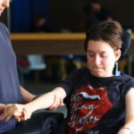 Alissa, a C4 quadriplegic patient, undergoing physical therapy with the assistance of a therapist, focusing on arm movement exercises. She is seated in a wheelchair, determined and focused on her rehabilitation