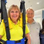 Dominique, a determined C6 quadriplegic patient, stands in a supportive harness during a therapy session, assisted by two Verita Neuro specialists and supported by her husband. The bright and modern therapy room reflects the advanced care and positivity driving her recovery through Epidural Stimulation and rehabilitation.