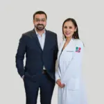 Dr. Nasir Majeed stands smiling at the camera, wearing a dark grey suit and glasses. He stands beside Dr. Beatriz Perez Hernandez who wears a white lab coat with the national flags of Mexico and Thailand embroidered on the sleeve, as she smiles at the camera too.