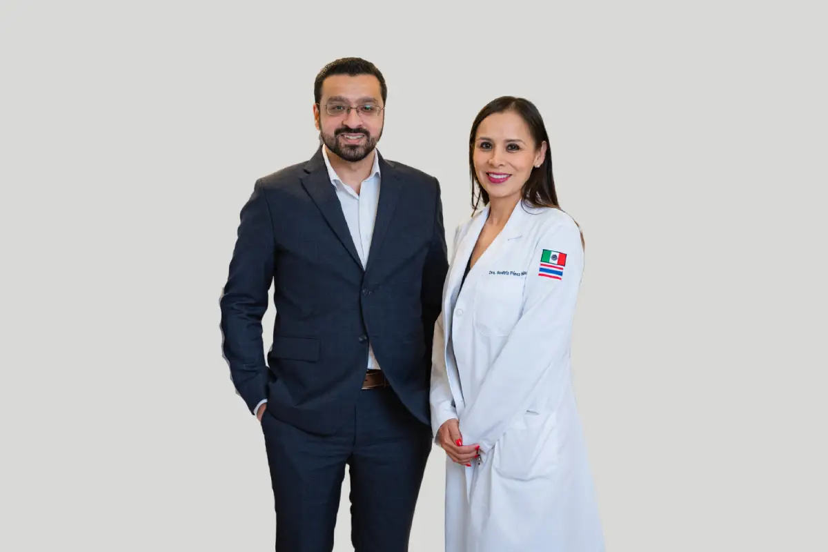 Dr. Nasir Majeed stands smiling at the camera, wearing a dark grey suit and glasses. He stands beside Dr. Beatriz Perez Hernandez who wears a white lab coat with the national flags of Mexico and Thailand embroidered on the sleeve, as she smiles at the camera too.