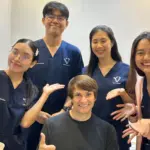 Igor sits in a wheelchair smiling, surrounded by four Verita Neuro team members wearing hospital scrubs, who are all leaning in and smiling for a group photo.