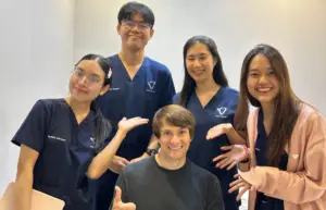 Igor sits in a wheelchair smiling, surrounded by four Verita Neuro team members wearing hospital scrubs, who are all leaning in and smiling for a group photo.