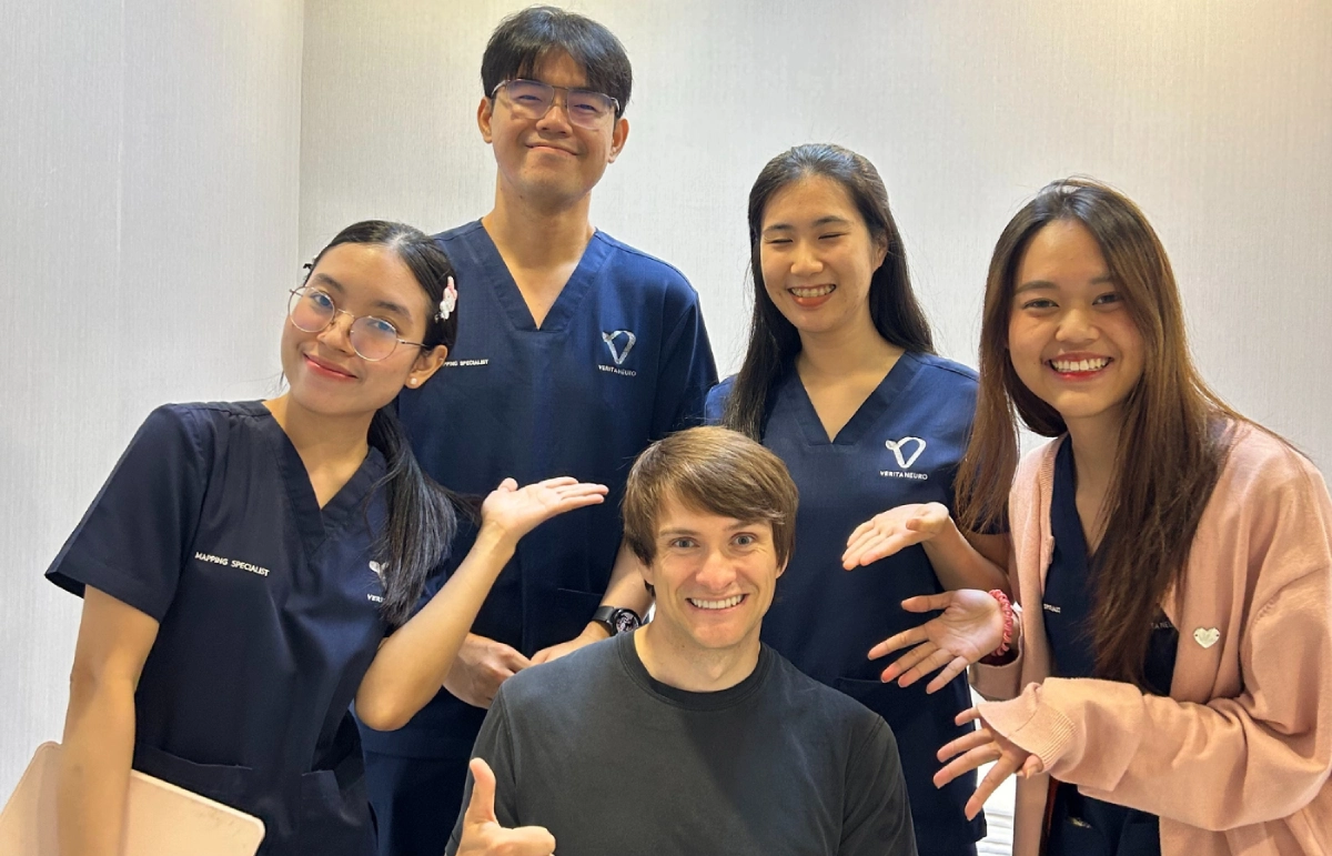 Igor sits in a wheelchair smiling, surrounded by four Verita Neuro team members wearing hospital scrubs, who are all leaning in and smiling for a group photo.
